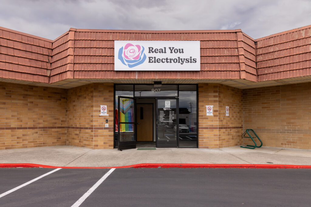 The front of our Vancouver WA location. The front double doors have a pride flag in the window, and there is an overhead sign showing the Real You Electrolysis logo.